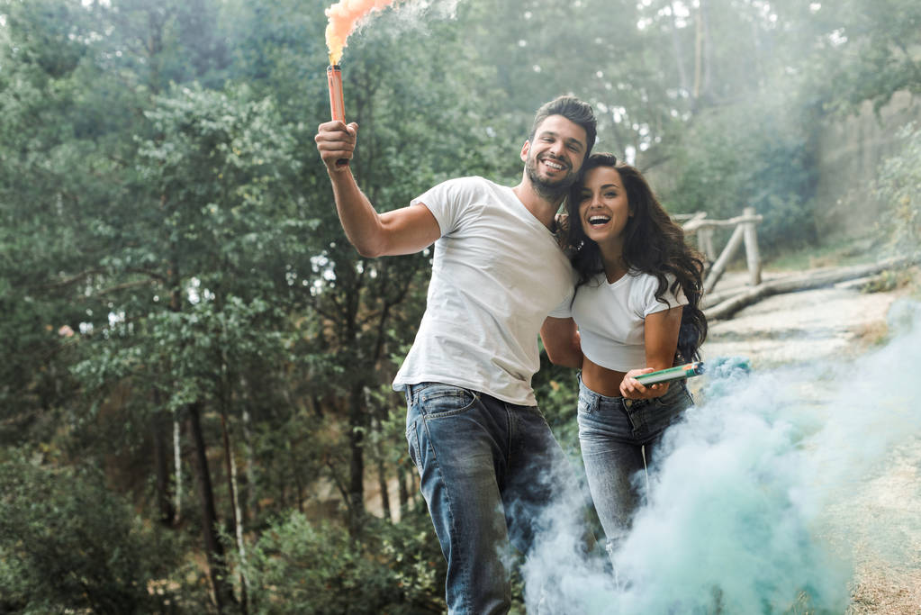 attractive woman and cheerful bearded man holding smoke bombs  - Photo, Image