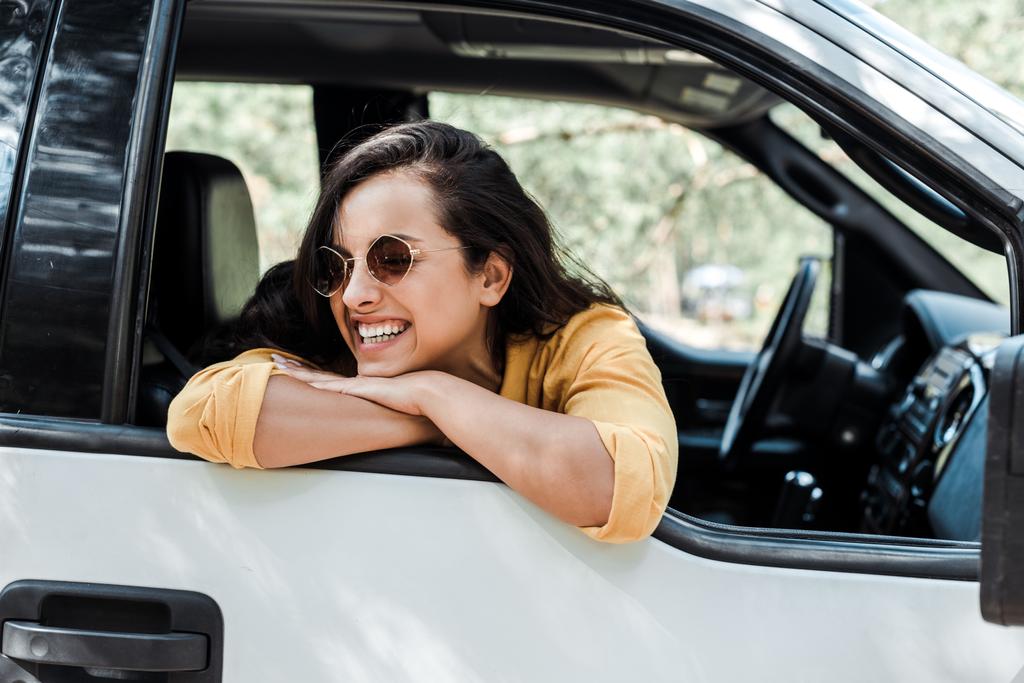 χαρούμενο κορίτσι στα γυαλιά ηλίου χαμογελώντας από το παράθυρο του αυτοκινήτου  - Φωτογραφία, εικόνα