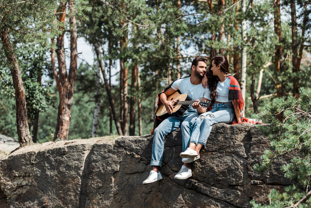bearded man playing acoustic guitar near woman in woods  - Photo, Image
