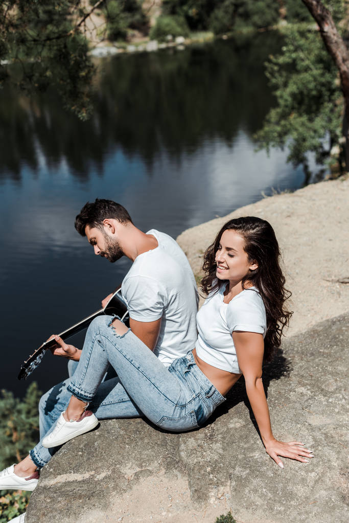 overhead view of man playing acoustic guitar near woman and lake  - Photo, Image