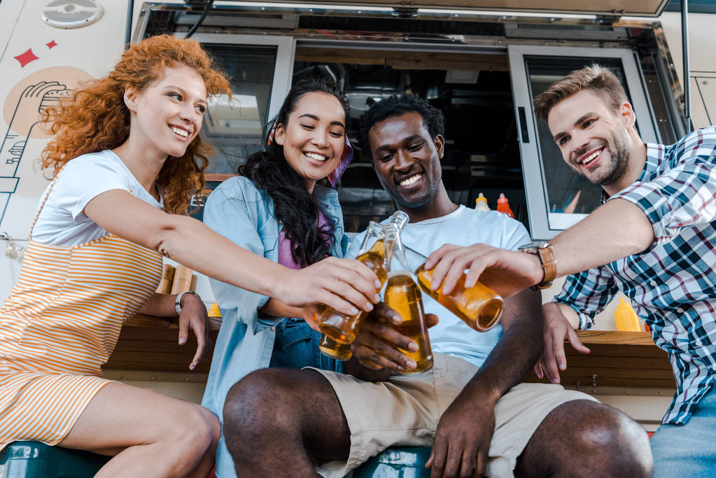 happy multicultural friends clinking bottles with beer near food truck   - Photo, Image