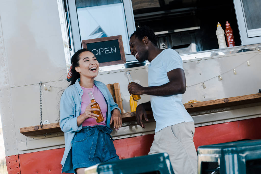 onnellinen aasialainen tyttö nauraa lähellä afrikkalainen amerikkalainen mies pullon olutta
  - Valokuva, kuva