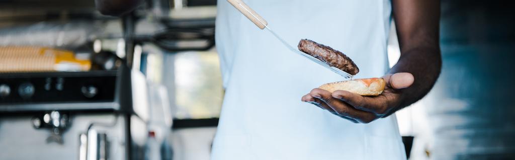 ハンバーガーを準備しながら、へらを持つアフリンアメリカ人男性のパノラマショット  - 写真・画像