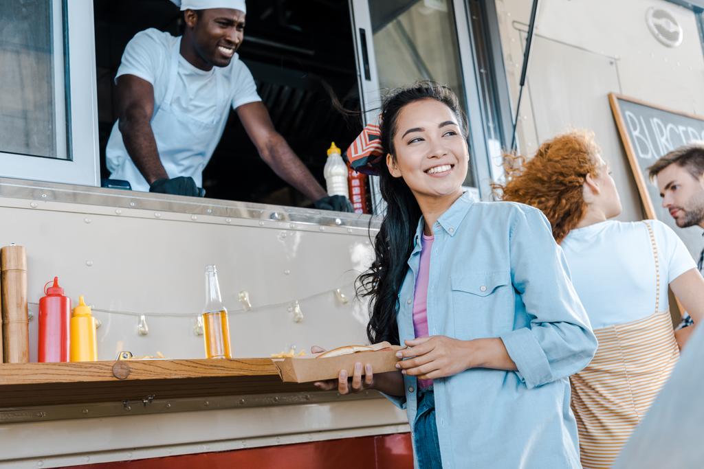 foyer sélectif de joyeuse fille asiatique tenant la plaque de carton près des clients et du chef dans un camion alimentaire
  - Photo, image