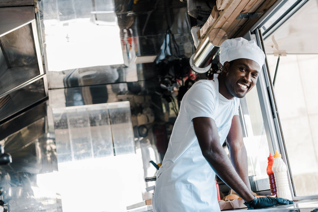 избирательный фокус счастливого африканского шеф-повара, улыбающегося в фургоне с едой
  - Фото, изображение