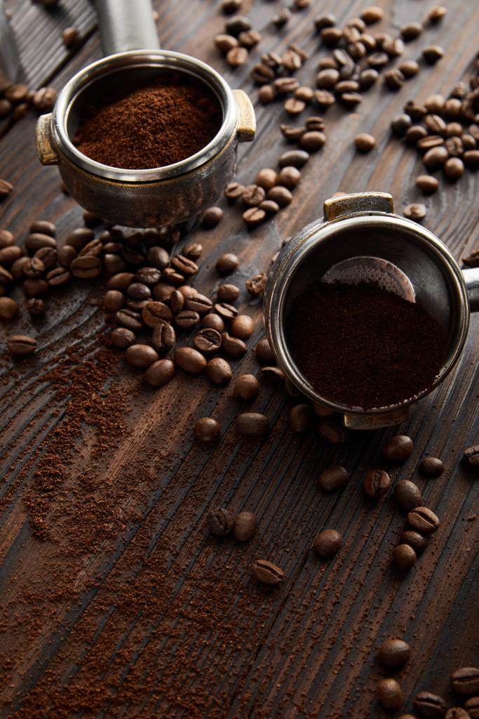 Portafilters filled with aromatic ground coffee on dark wooden surface with coffee beans - Photo, Image