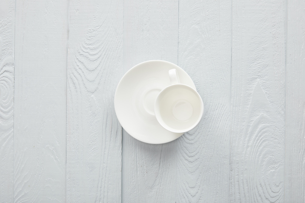 Порожня біла чашка з блюдцем на білій дерев'яній поверхні
 - Фото, зображення