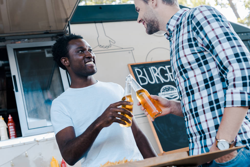 baixo ângulo de visão de homens multiculturais felizes brindar garrafas de cerveja
  - Foto, Imagem