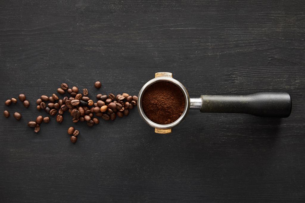 Bovenaanzicht van filterhouder met koffie op donker houten oppervlak met verspreide koffiebonen - Foto, afbeelding