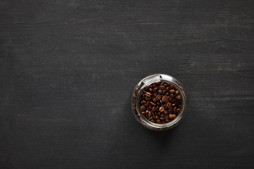 Skleněná nádobka s kávovými fazolemi na tmavém dřevěném povrchu - Fotografie, Obrázek