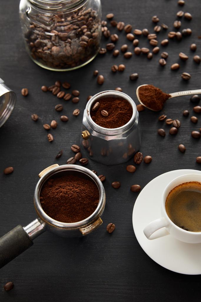 Καφετιέρα θερμοσυσκευή κοντά σε φλιτζάνι καφέ, portafilter, κουτάλι και γυάλινο βάζο σε σκοτεινή ξύλινη επιφάνεια με κόκκους καφέ - Φωτογραφία, εικόνα