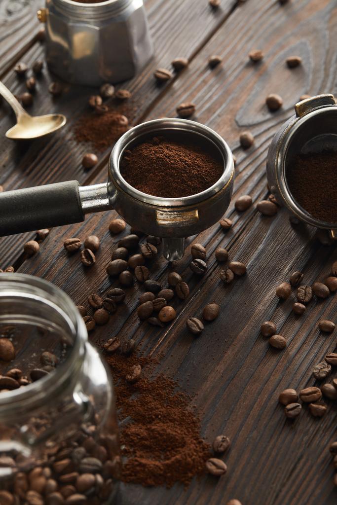 Portafilter near spoon, geyser coffee maker and glass jar with coffee beans on dark wooden surface - Photo, Image