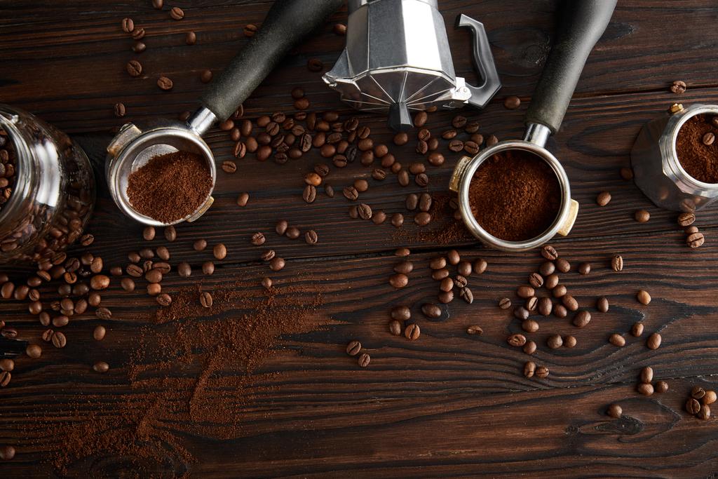 Top uitzicht van geiser koffie maker tussen portafilters en glazen pot op donker houten oppervlak met koffiebonen - Foto, afbeelding
