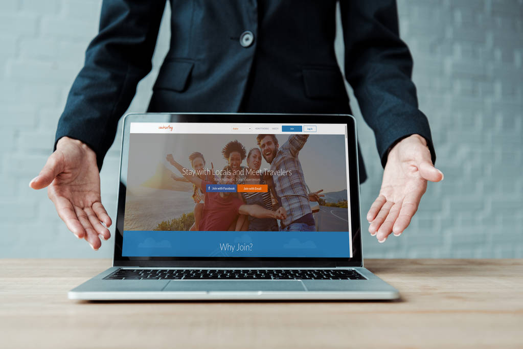 キエフ, ウクライナ - 8月 5, 2019: 画面上のカウチサーフィンのウェブサイトを持つラップトップの近くでジェスチャー女性のトリミングビュー  - 写真・画像
