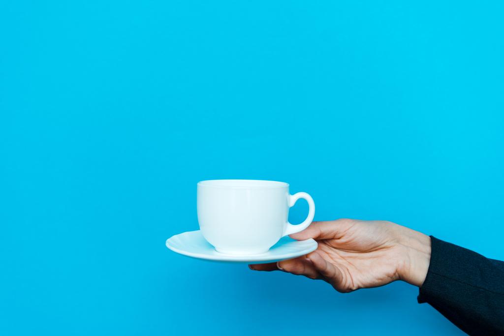 cropped view of woman holding saucer and cup on blue - Photo, Image