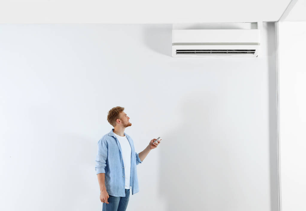 Nuori mies käyttää ilmastointilaitetta kaukosäätimellä sisätiloissa. Tekstitila
 - Valokuva, kuva