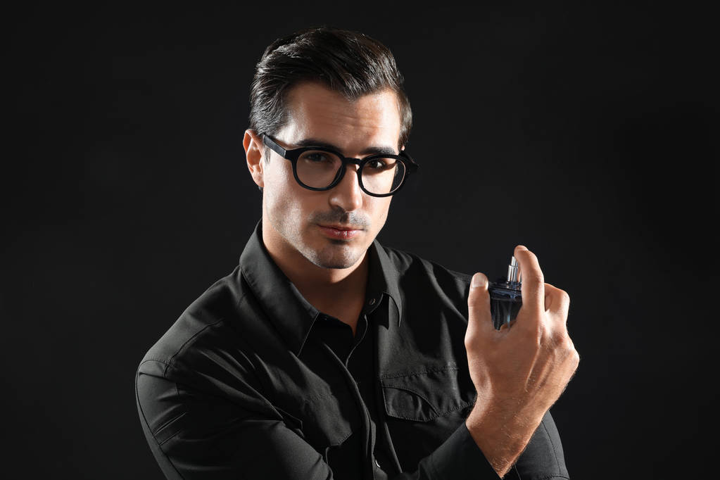schöner junger Mann in Brille mit Parfüm auf schwarzem Hintergrund - Foto, Bild