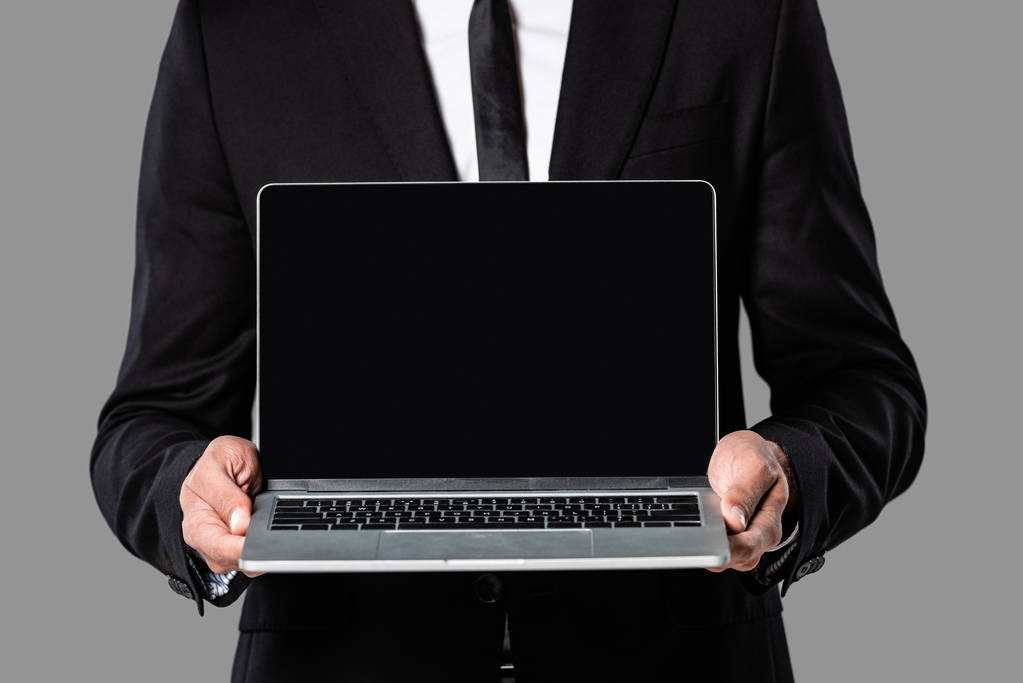 обрезанный вид бизнесмена в черном костюме, показывающий ноутбук с пустым экраном, изолированным на сером
 - Фото, изображение