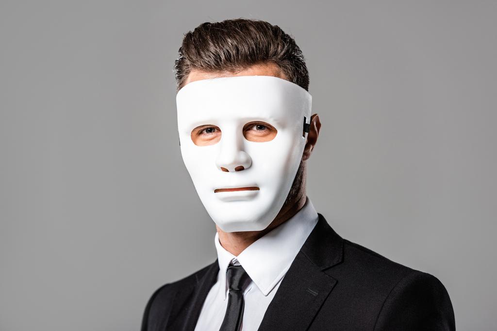 μυστηριώδης επιχειρηματίας με μαύρο κοστούμι και μάσκα απομονώνεται σε γκρι - Φωτογραφία, εικόνα