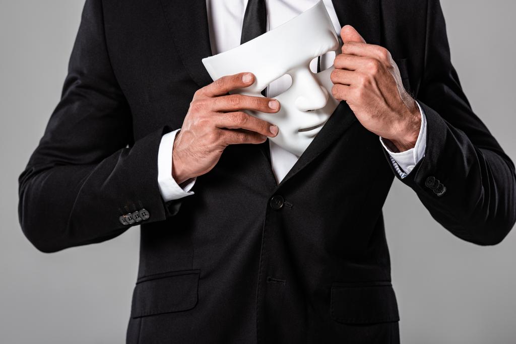 vue partielle de l'homme d'affaires en costume noir tenant masque blanc isolé sur gris
 - Photo, image