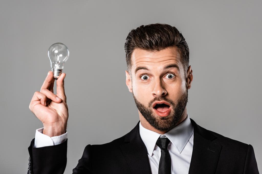 shocked businessman in black suit holding light bulb isolated on grey - Photo, Image