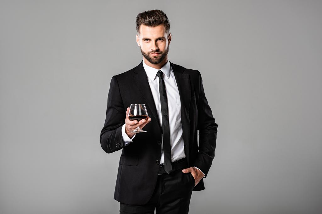 успешный бизнесмен в черном костюме держит стакан с виски, изолированным на сером
 - Фото, изображение