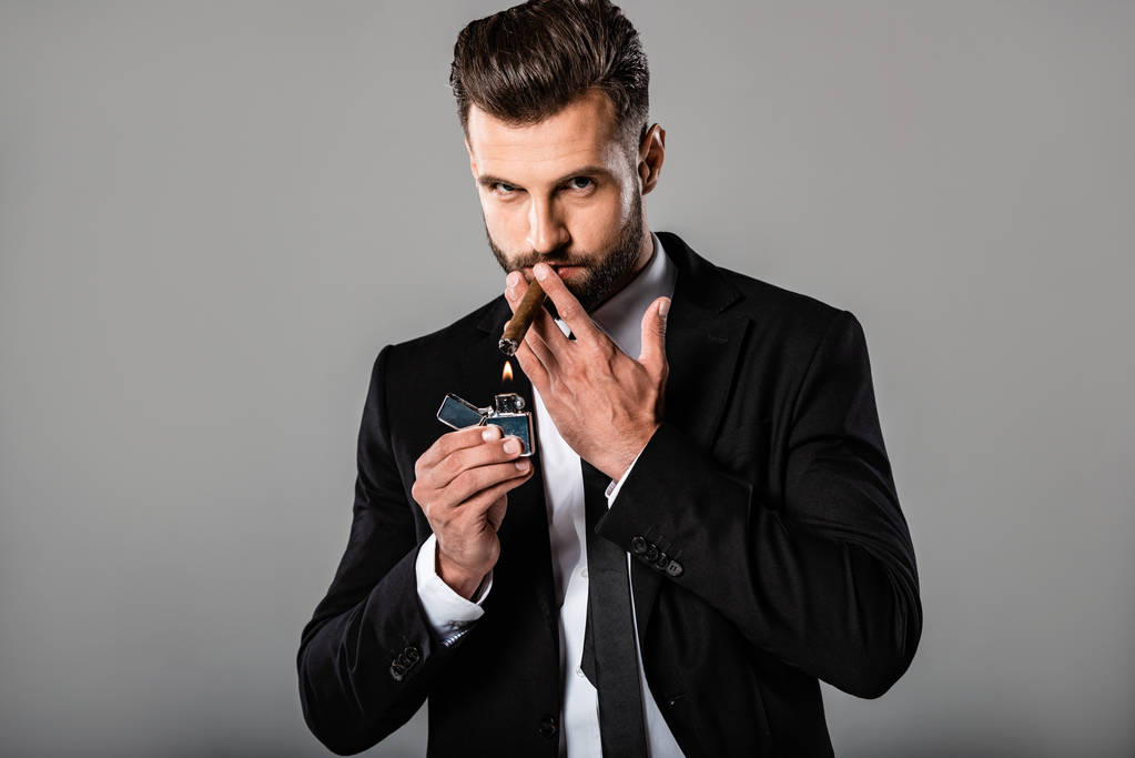 впевнений бізнесмен в чорному костюмі освітлює сигару ізольовано на сірому
 - Фото, зображення