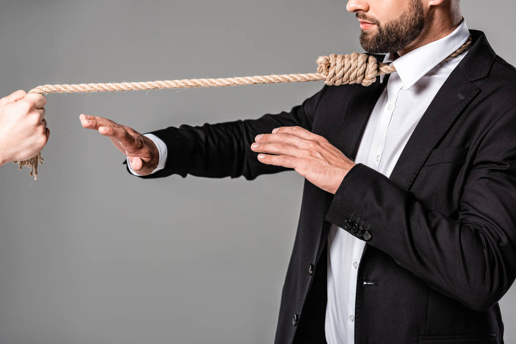 cropped view of businessman in black suit with noose on neck showing stop gesture to murderer with rope isolated on grey - Photo, Image