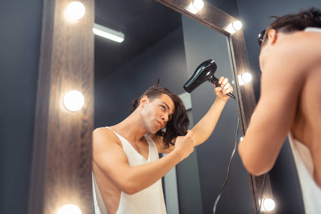 Приємний красивий чоловік сушить довге волосся
 - Фото, зображення