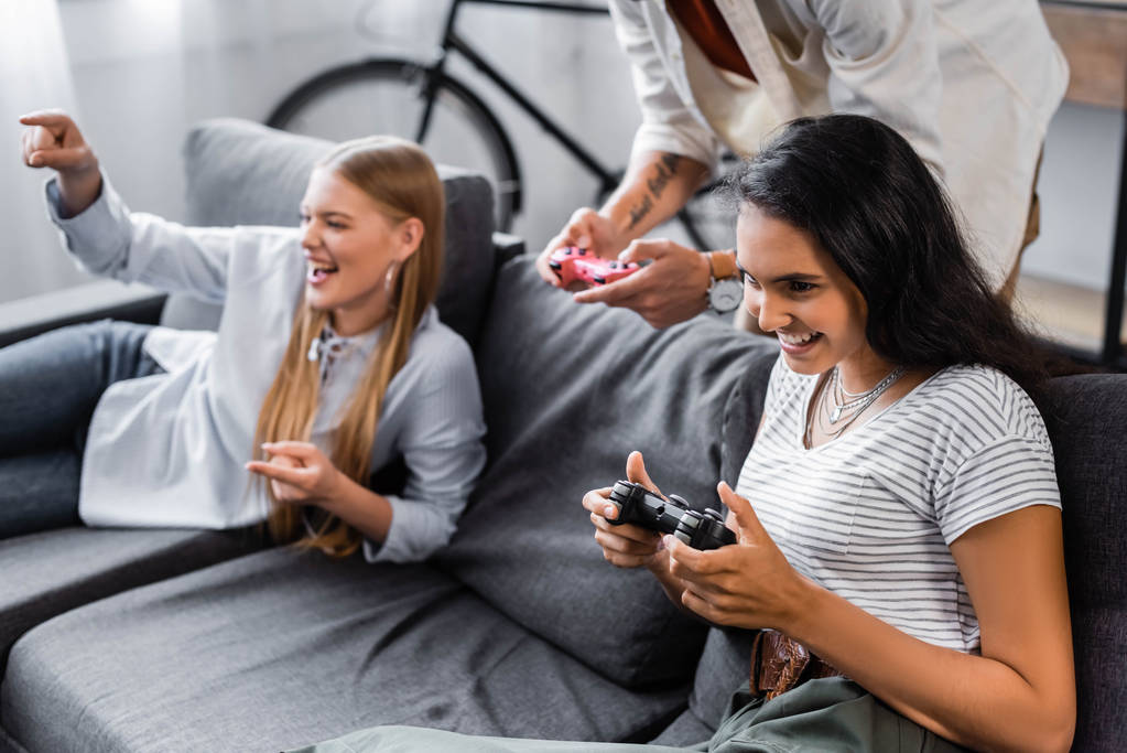 Київ, Україна-10 липня 2019: багатокультурні друзі сидять на дивані і грають у відео-ігри в квартирі  - Фото, зображення