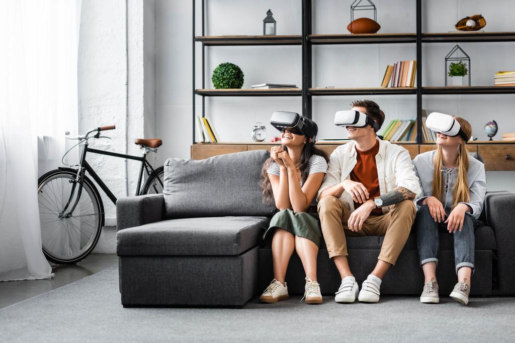 smiling multicultural friends with virtual reality headsets sitting on sofa  - Photo, Image