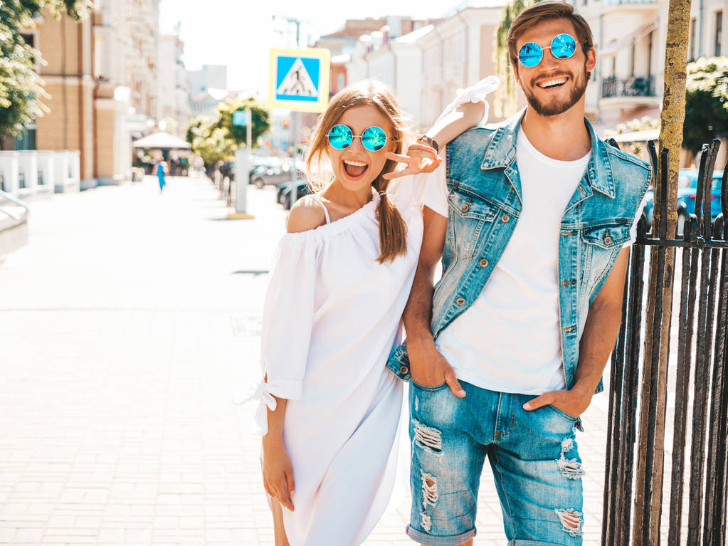 lächelnde schöne Mädchen und ihr schöner Freund posieren auf der Straße. Frau in lässigem Sommerkleid und Mann in Jeans. fröhliches Paar Familie hat Spaß mit Sonnenbrille - Foto, Bild