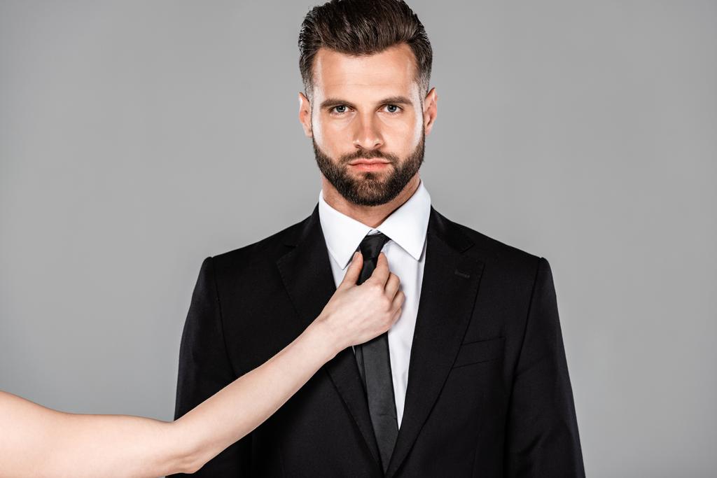 灰色で隔離された黒いスーツでビジネスマンにネクタイを結ぶ女性 - 写真・画像