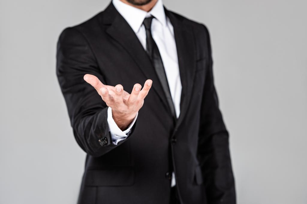 частичный взгляд бизнесмена в черном костюме с рукой попрошайки, изолированной на сером
 - Фото, изображение