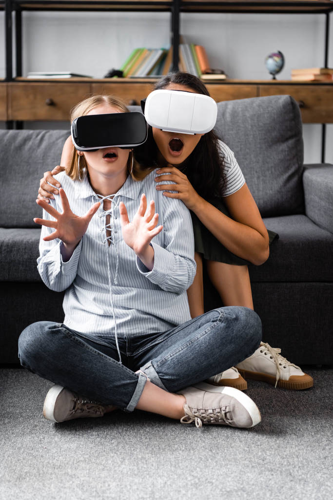 monikulttuurinen ystäviä virtuaalitodellisuus kuulokkeet istuu lattialla asunnossa
  - Valokuva, kuva