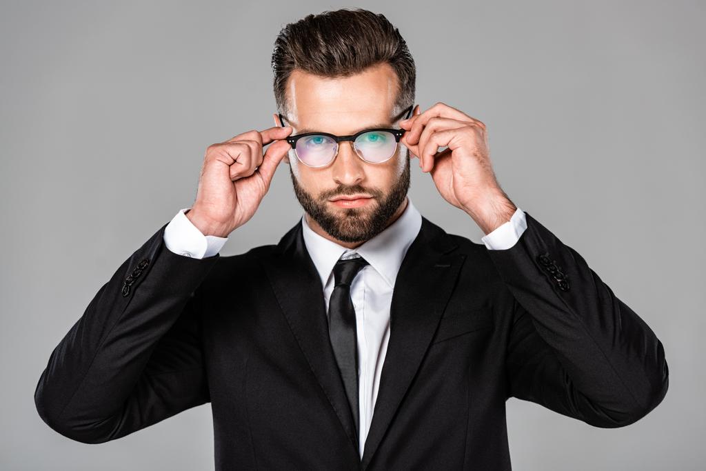 successful businessman in black suit touching glasses isolated on grey - Photo, Image