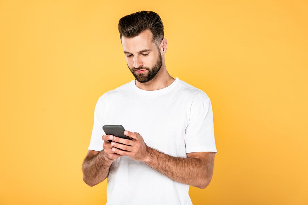 handsome man in white t-shirt using smartphone isolated on yellow - Photo, Image