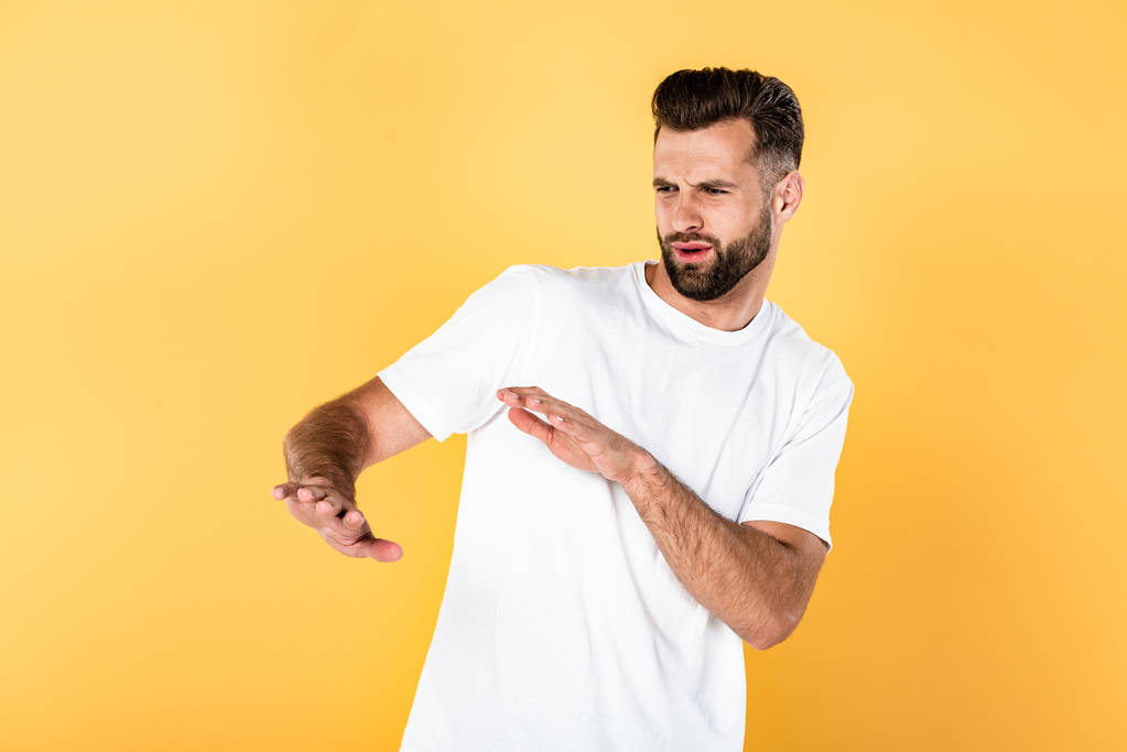 przystojny mężczyzna w białym t-shirt ciążący z rękami wyizolowanymi na żółto - Zdjęcie, obraz