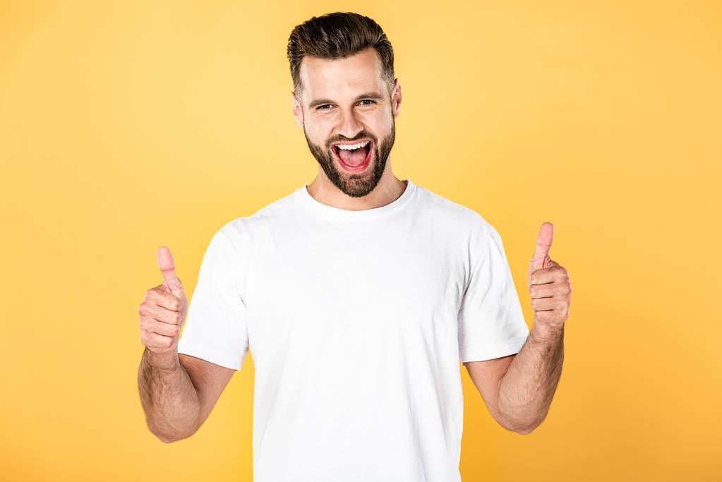 excitado hombre guapo en camiseta blanca mostrando pulgares hacia arriba aislado en amarillo
 - Foto, Imagen