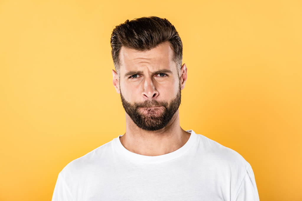 confused handsome man in white t-shirt grimacing isolated on yellow - Photo, Image