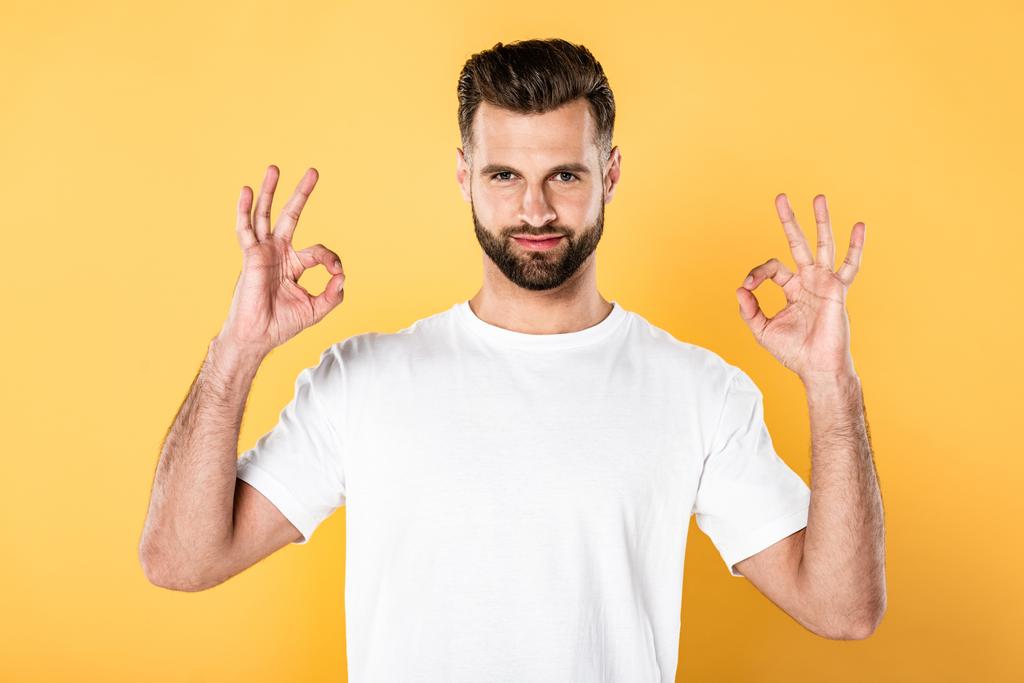 handsome man in white t-shirt showing ok signs isolated on yellow - Photo, Image