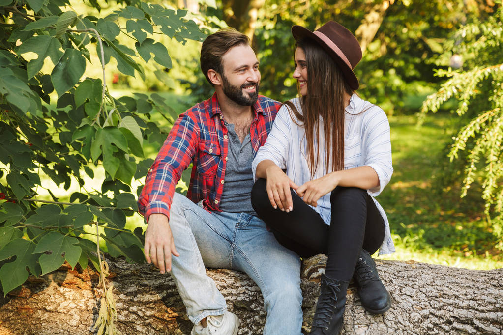 Immagine di coppia attraente uomo e donna che sorridono seduti su un albero nel parco verde
 - Foto, immagini