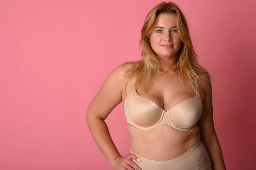 Mooie overgewicht vrouw in beige badpak op roze achtergrond - Foto, afbeelding