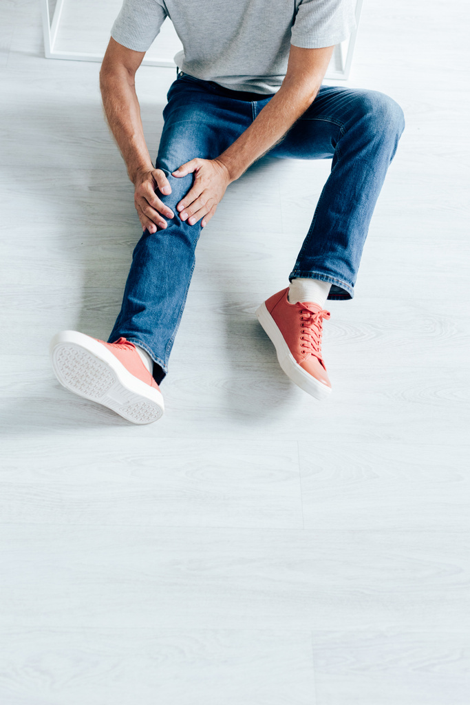 oříznutý pohled muže v trička cítí bolest v koleni v bytě  - Fotografie, Obrázek