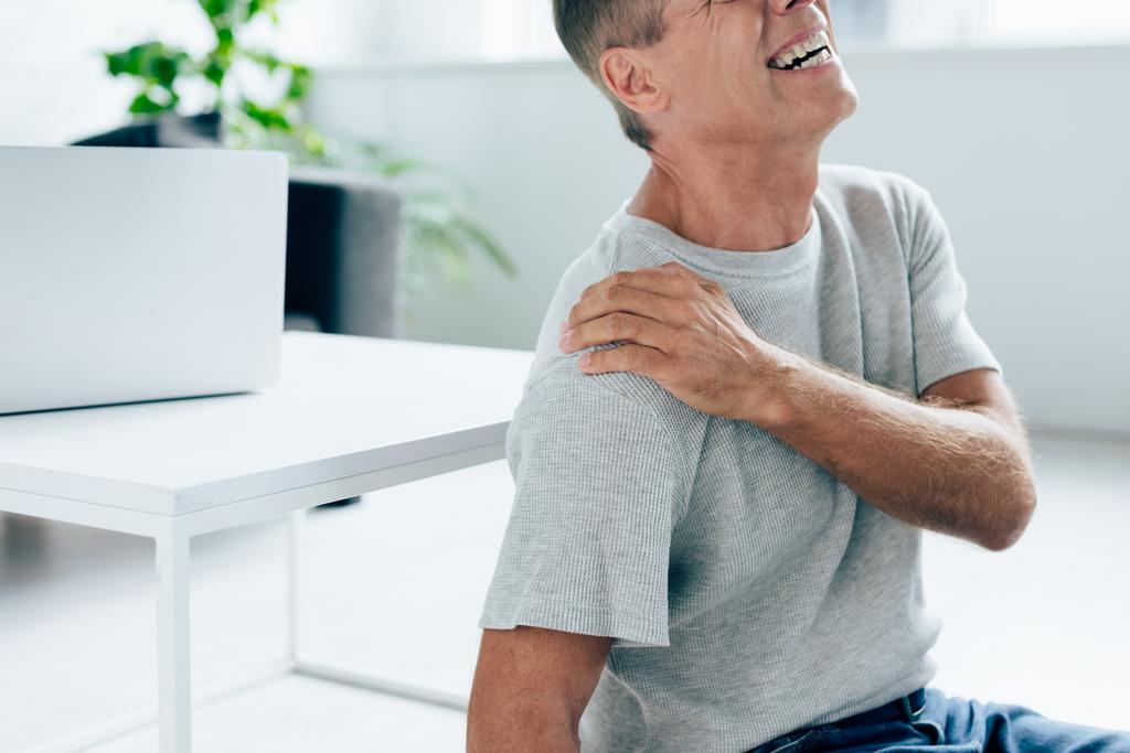 ostříhané zobrazení pohledného muže v tričku pocit bolesti v rameni v bytě  - Fotografie, Obrázek