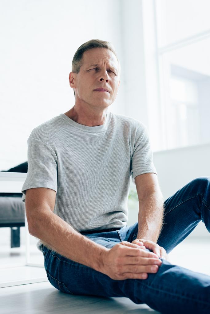 schöner Mann im T-Shirt spürt Schmerzen im Knie in Wohnung  - Foto, Bild