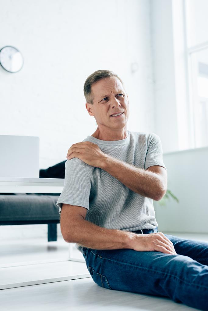 handsome man in t-shirt feeling pain in shoulder in apartment  - Photo, Image