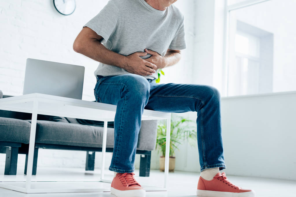 cropped view of man in t-shirt with stomachache in apartment  - Photo, Image