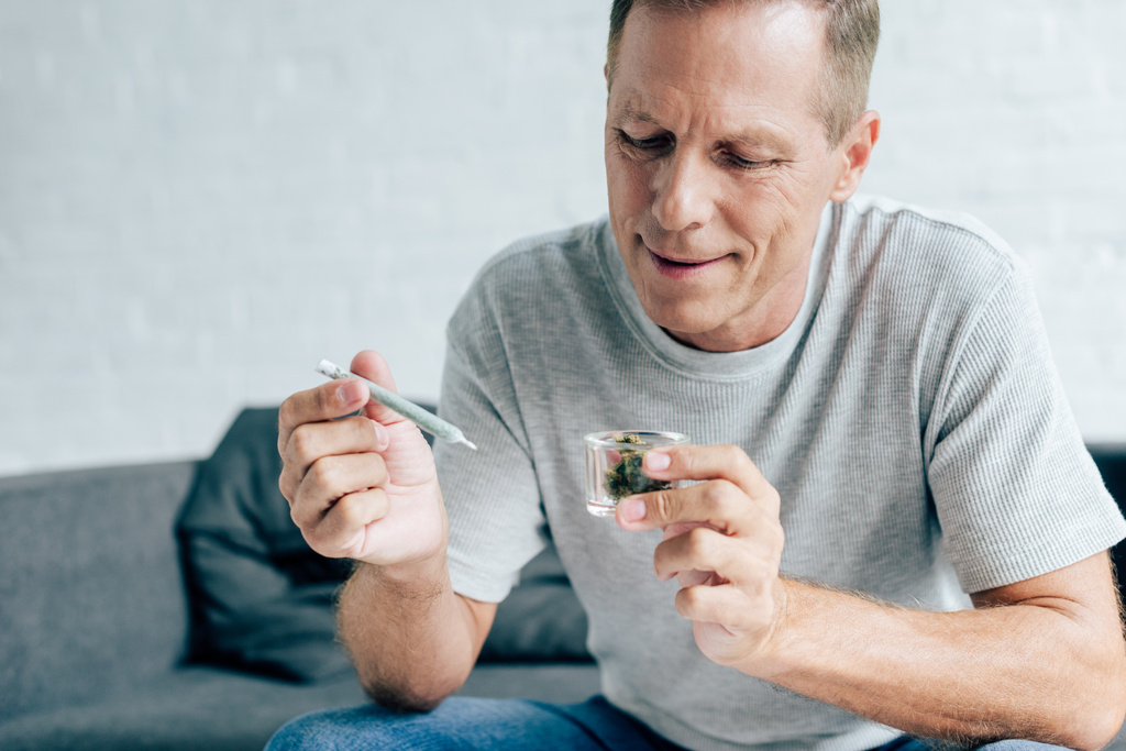handsome man in t-shirt holding blunt and medical cannabis - Photo, Image