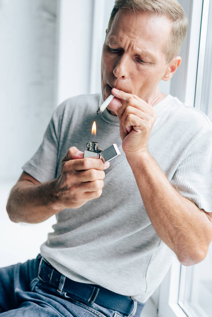 handsome man lighting up blunt with medical cannabis in apartment  - Photo, Image